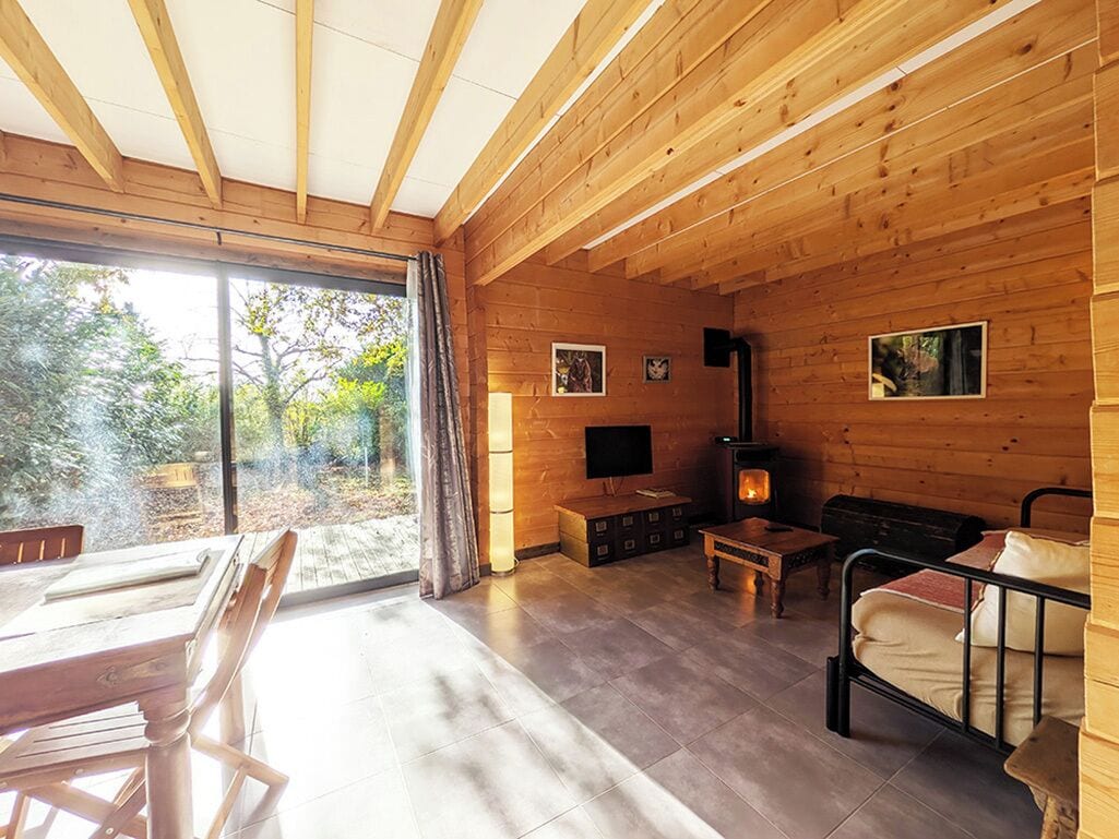 L’intérieur d’un chalet en bois comprend une cheminée, un téléviseur et un coin repas avec une table et des chaises.