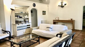 A living room with a sofa, a glass coffee table, a bookshelf, and a dining table. - Single storey villa, 4 bedrooms, swimming pool, near the beaches of the Gulf of Saint Trop (Grimaud)