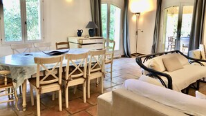 A dining area with a round table and chairs, a sofa, and a lamp. - Single storey villa, 4 bedrooms, swimming pool, near the beaches of the Gulf of Saint Trop (Grimaud)