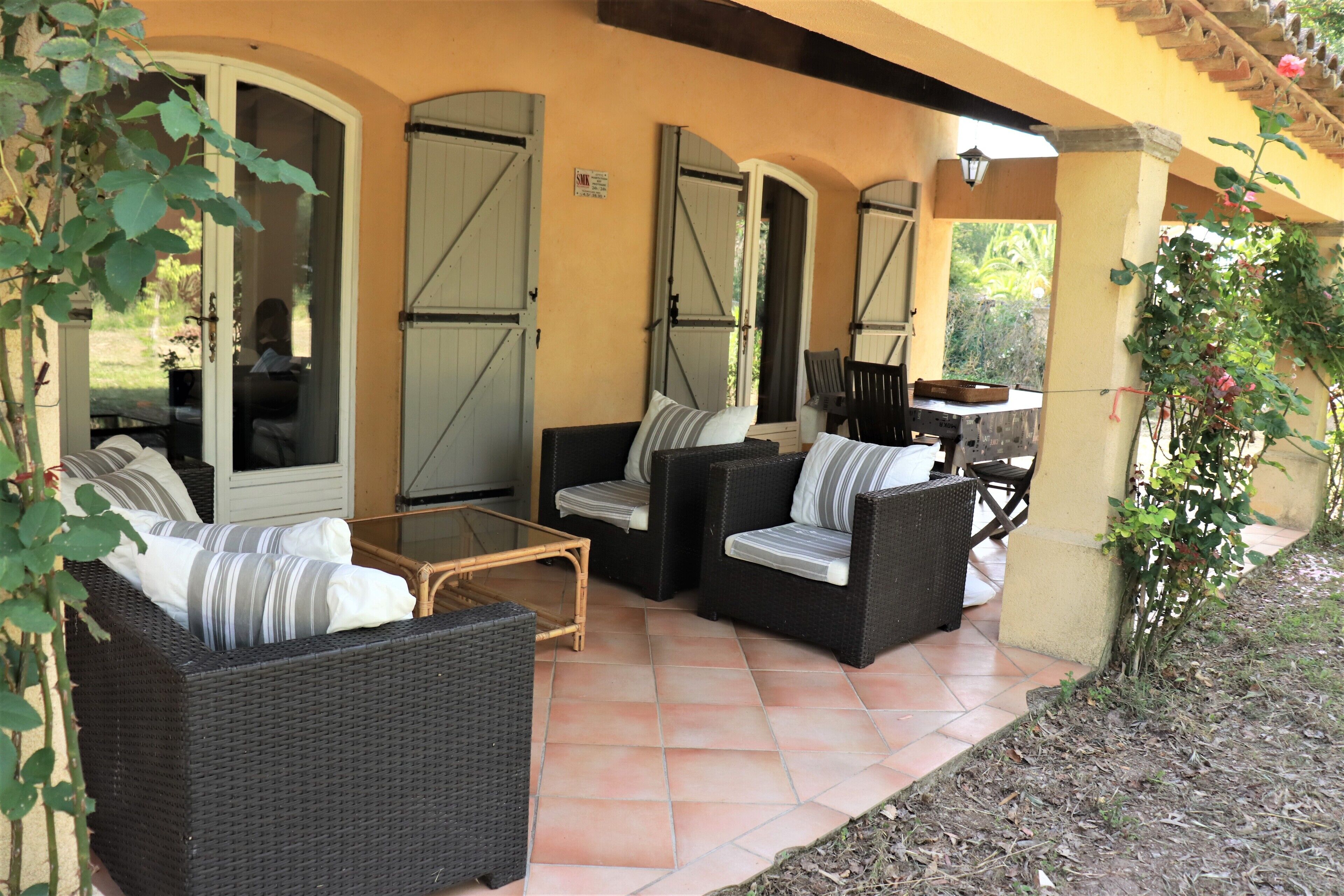 An outdoor patio with wicker furniture, a glass table, and a pergola with climbing plants.