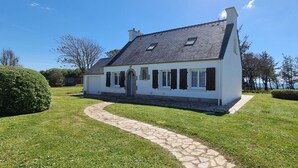 A house with a stone pathway leading to the entrance, surrounded by well-maintained grass and trees. - Exceptional location 2 steps from the sea for this single storey house (Trégunc)