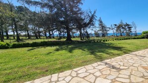 A well-maintained lawn with a stone pathway leading to a seating area, surrounded by trees and a view of the sea. - Exceptional location 2 steps from the sea for this single storey house (Trégunc)