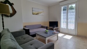 A living room with a grey sofa, a coffee table with a green object, a TV, and a sliding glass door leading outside. - Exceptional location 2 steps from the sea for this single storey house (Trégunc)