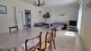 A dining area with a round table, chairs, and a chandelier. There is a sofa and a television in the living area. - Exceptional location 2 steps from the sea for this single storey house (Trégunc)