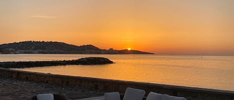 A sunset view from a wooden deck with wicker furniture and a stone wall.