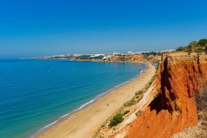 A coastal view with a sandy beach, a cliff, and a distant cityscape.