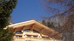 Um chalé de madeira com varanda, rodeado por neve e árvores.