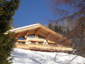 Eine Holzhütte mit Balkon, umgeben von Schnee und Bäumen.