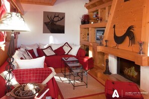 Ein gemütliches Wohnzimmer mit Kamin, roten und weißen Möbeln sowie einer Holzbalkendecke.