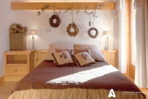 Ein Schlafzimmer mit einem Holzkopfteil, einem Bett mit brauner Bettdecke, mehreren Kissen, zwei Nachttischen mit Lampen und einem Korb auf der linken Seite.