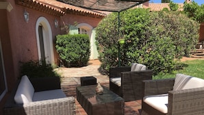 Un patio exterior con mobiliario de mimbre y piso de baldosas.