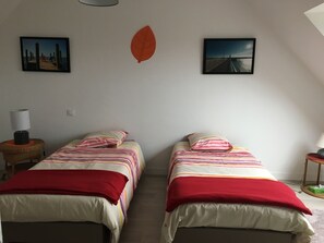 Una habitación con dos camas, cada una con ropa de cama a rayas y almohadas rojas, una lámpara en una mesita de noche y dos cuadros en la pared.