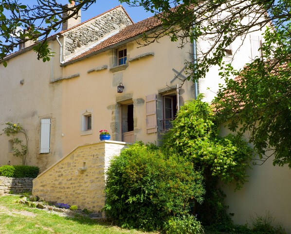 A traditional stone house with a sloped roof, a small porch, and a window with shutters.