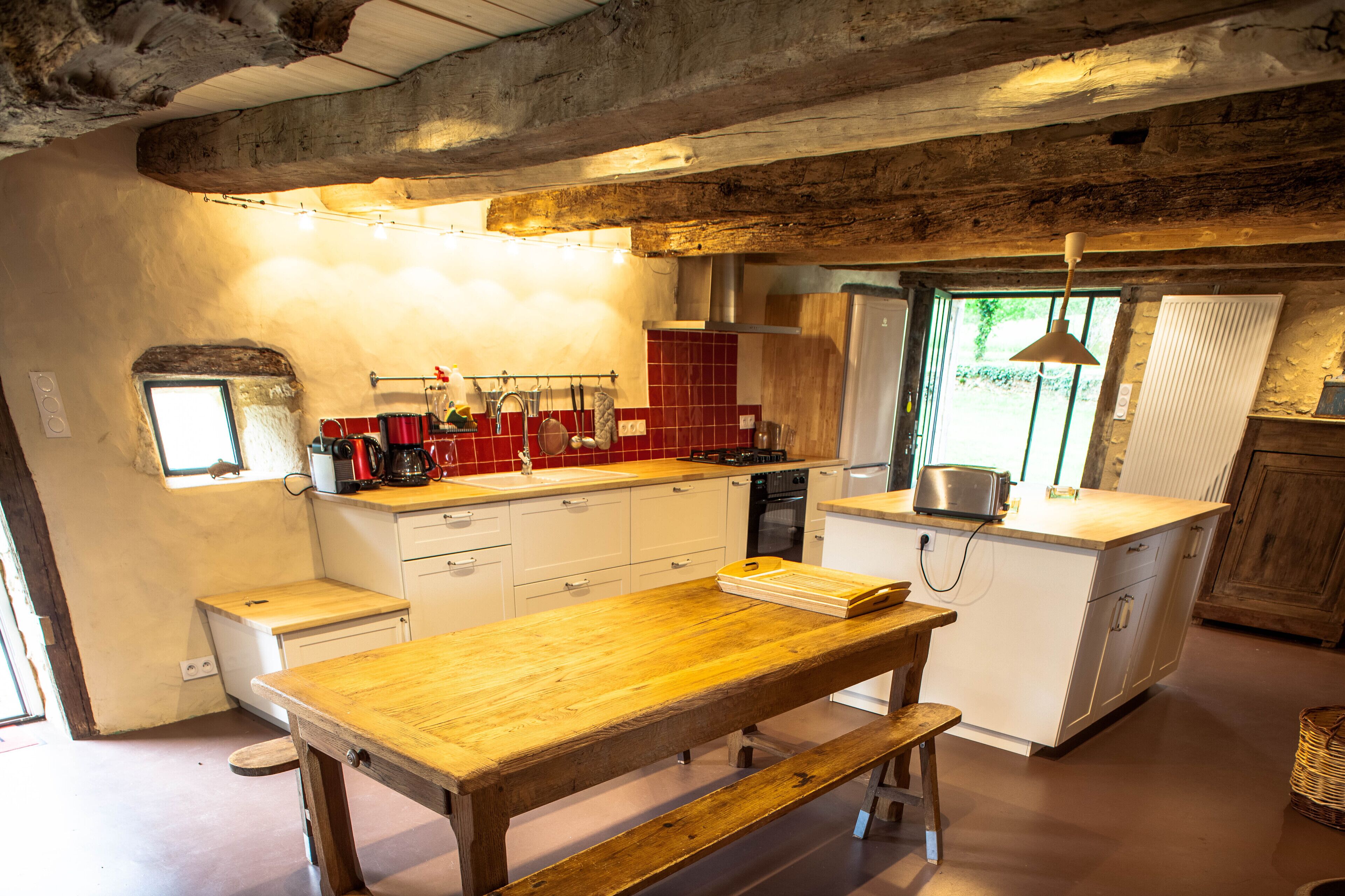 A kitchen with a wooden table, white cabinets, and a window with a view of greenery.