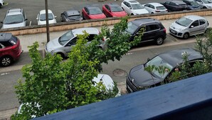 Un port de plaisance où sont amarrés de nombreux bateaux, un parking rempli de voitures et une vue sur des montagnes lointaines.