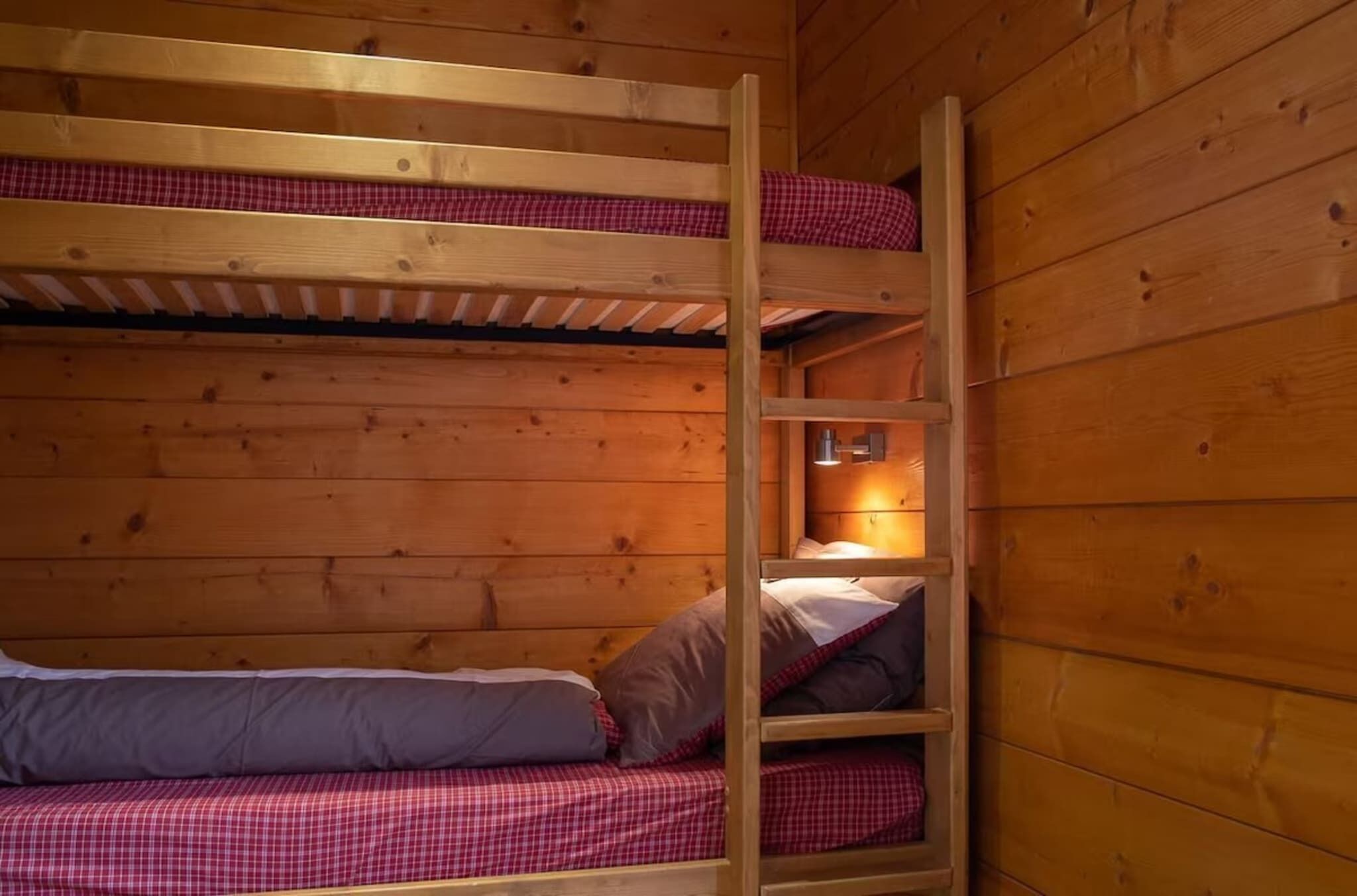 Une chambre avec un lit superposé, des murs en bois et une petite étagère sur laquelle se trouve une lampe.