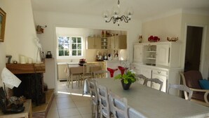 A spacious dining area with a large table, multiple chairs, and a chandelier. There is a kitchen in the background with white cabinets and various kitchen items. - CHARMING, BRIGHT 8-PERSON HOUSE CLOSE TO THE BEACH AND SUSCINIO CASTLE (Sarzeau)