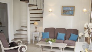 A living room with a staircase, a sofa with blue cushions, a white armchair, a small table with a lamp, and a painting on the wall. - CHARMING, BRIGHT 8-PERSON HOUSE CLOSE TO THE BEACH AND SUSCINIO CASTLE (Sarzeau)