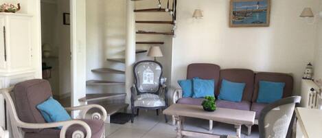 A living room with a sofa, two armchairs, a coffee table, and a spiral staircase.