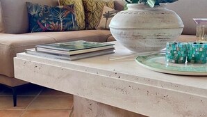 Ein modernes Wohnzimmer mit einem beigen Sofa, einer großen weißen Vase und einem Glastisch.