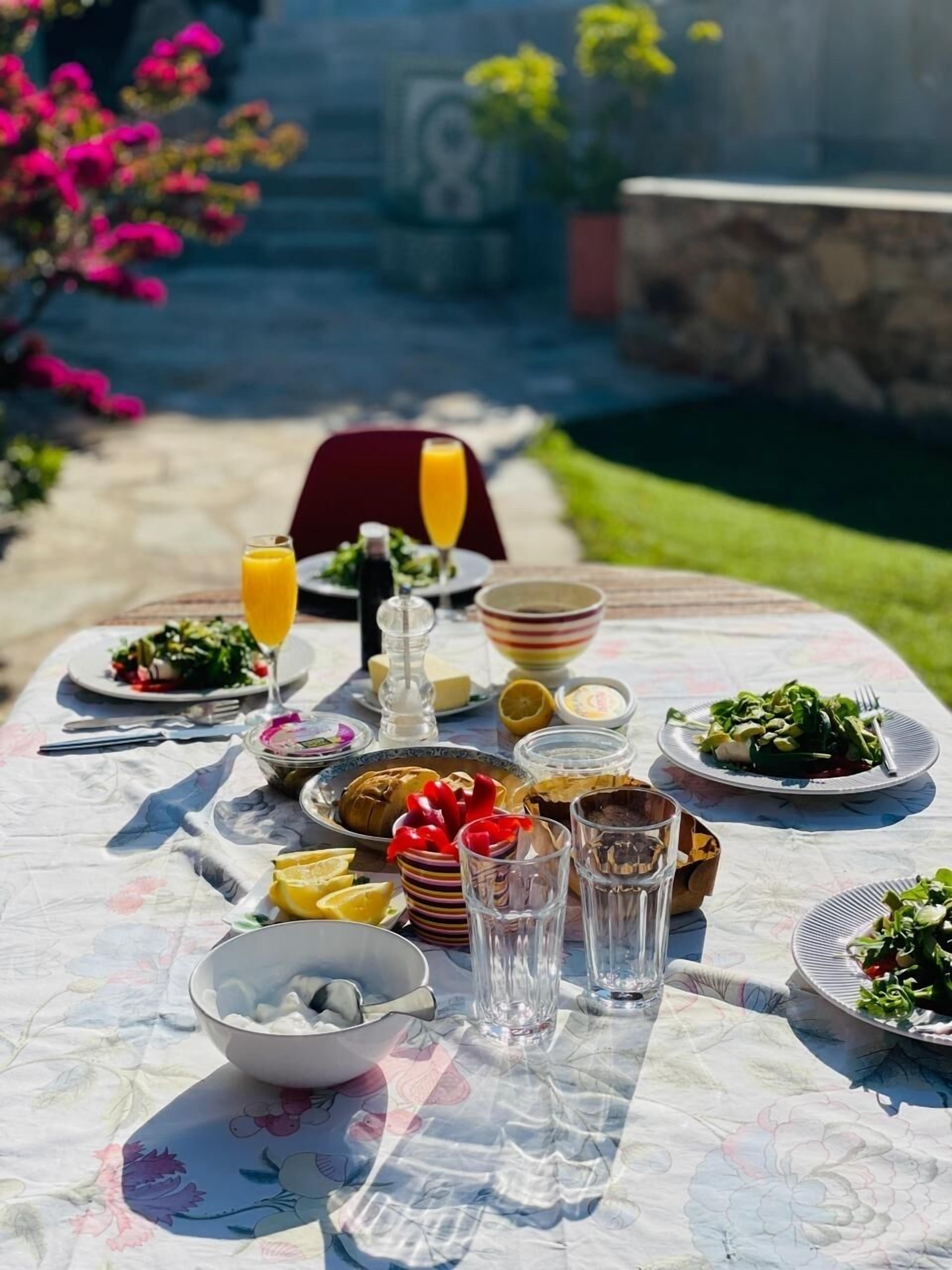 An outdoor dining table with various dishes, glasses, and condiments.