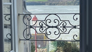 A balcony with a wrought iron railing overlooking a body of water and distant hills. - Villa with sea view and terrace, very sunny south-west exposure (Saint-Suliac)