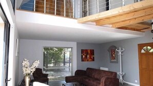 A spacious living area with a high ceiling, a staircase to an upper level, and a large window providing natural light. - Villa with sea view and terrace, very sunny south-west exposure (Saint-Suliac)