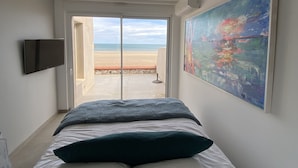 Une chambre avec un lit, un tableau, une télévision et une vue sur la plage.