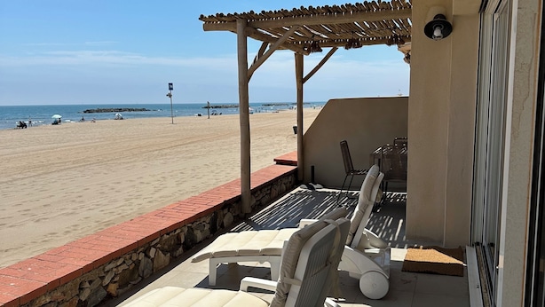 Une terrasse couverte avec des chaises longues et vue sur la plage.