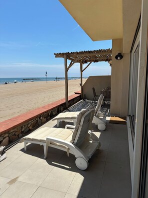 Une terrasse couverte avec des chaises longues et vue sur la plage.