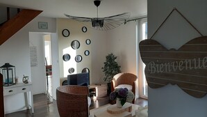 A modern living room with a high ceiling, a unique ceiling fan, and a 'Bienvenue' welcome sign. - Prepare your future vacations... all in Roz! (Perros-Guirec)