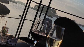 A table with two wine glasses and a bowl of nuts, overlooking a body of water with a distant shoreline and a clear sky. - Prepare your future vacations... all in Roz! (Perros-Guirec)