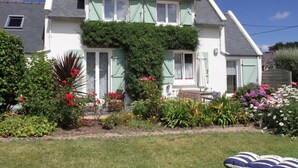 A two-story house with a green ivy-covered wall, a front porch, and a garden with various plants and flowers. - Prepare your future vacations... all in Roz! (Perros-Guirec)