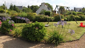 A garden with a swing set, a bench, and a red toy. - Prepare your future vacations... all in Roz! (Perros-Guirec)