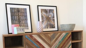 A wooden cabinet with a chevron-patterned front, two framed pictures, a white vase, a pink clock, and a woven basket.