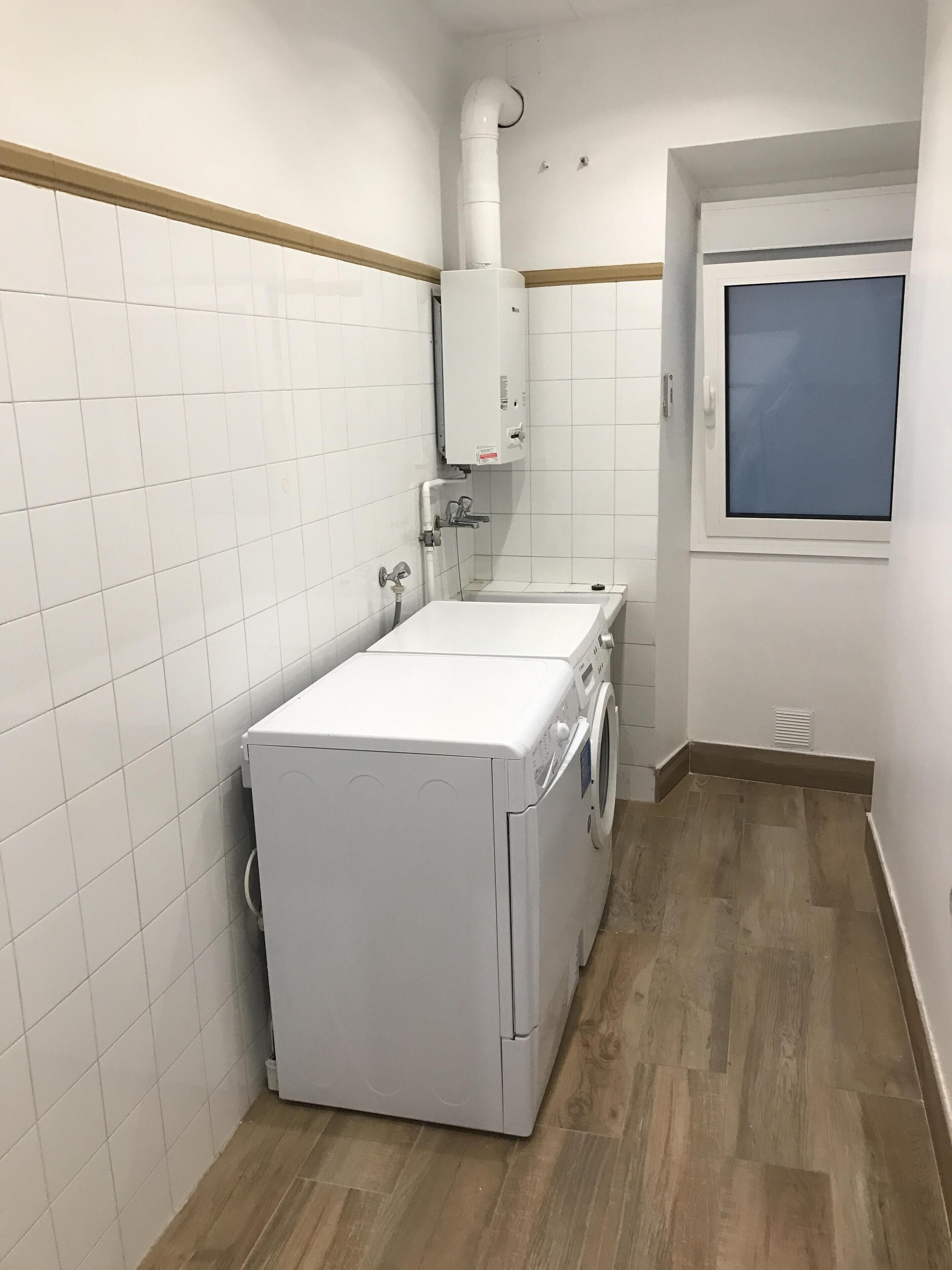 A compact laundry room with a washing machine and dryer, white tiled walls, and a wooden floor.