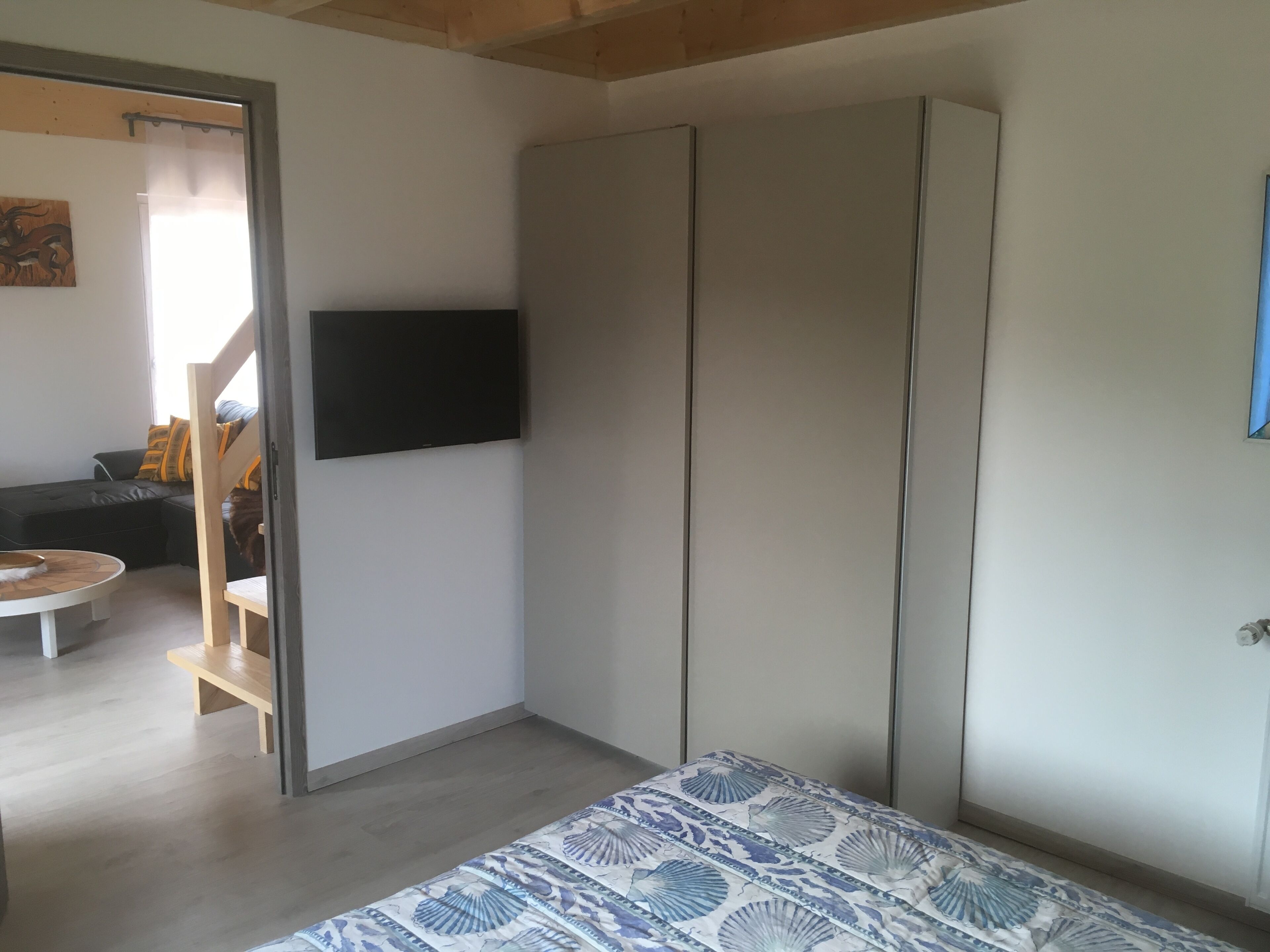 Ein Schlafzimmer mit Bett, Kleiderschrank, Wand-Fernseher und einer Holzbank.