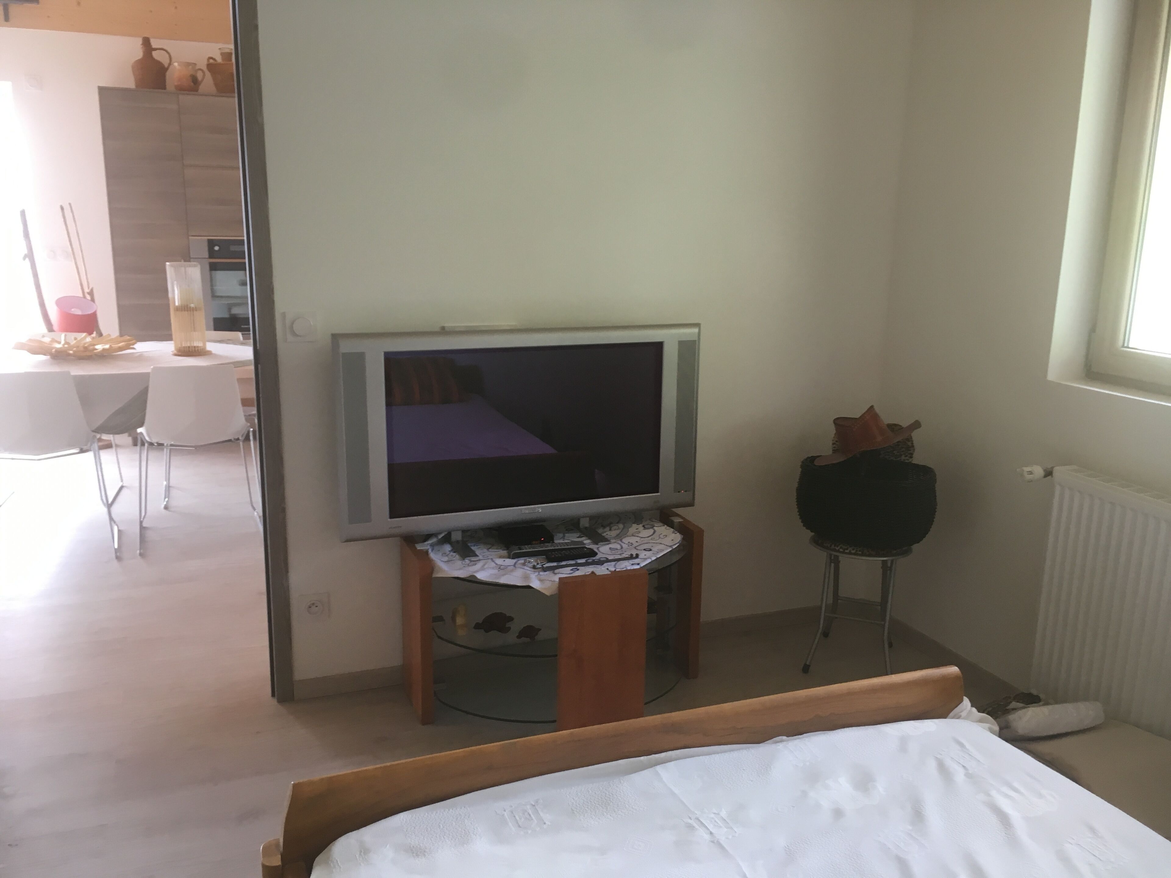 A bedroom with a bed, a television on a stand, a small table with a laptop, and a window.