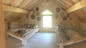 Ett mysigt sovrum på vinden med två sängar i trä, ett takfönster och en samling hattar på väggen.