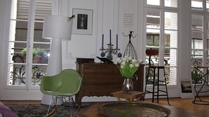 A room with a green chair, a wooden table, a vase with flowers, a lamp, and a framed picture on the wall.