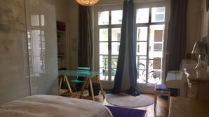A bedroom with a bed, a desk, a chair, and a window with curtains.