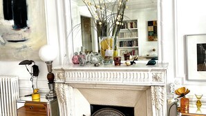 A room with a fireplace, a large mirror, a radiator, a wooden floor, and a bookshelf.