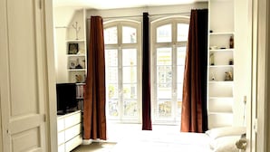 A bedroom with a bed, a dresser, a TV, and a window with curtains.