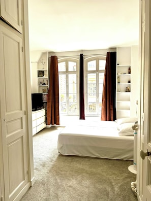 A bedroom with a bed, a dresser, a TV, and a window with curtains.