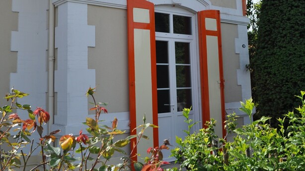 En byggnad med en vit fasad, orange detaljer och en framträdande entré med en glasdörr.