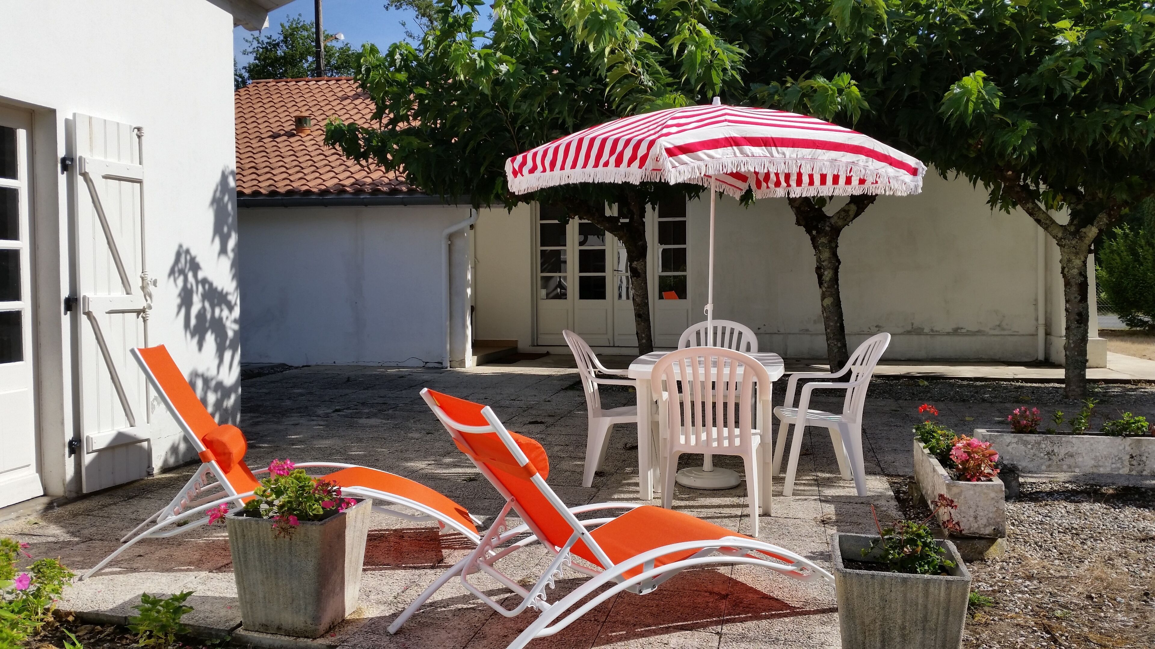 An outdoor seating area with a table and chairs, a striped umbrella, and potted plants.