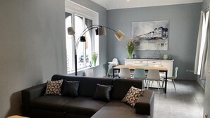 A modern living room with a sectional sofa, a dining area with a white table and chairs, and a kitchen in the background.