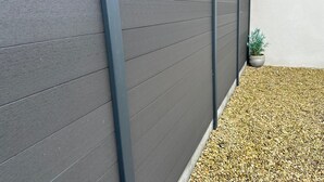 A modern building with a dark grey exterior wall and a metal fence.