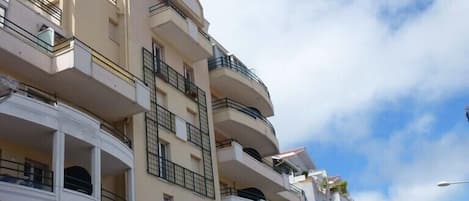 Un edificio residencial de varios pisos con balcones, cielo despejado y algunas palmeras.