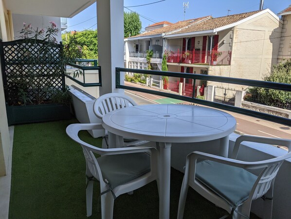 Un balcón con una mesa redonda y cuatro sillas, piso de césped artificial verde y vista a un edificio con barandillas rojas.